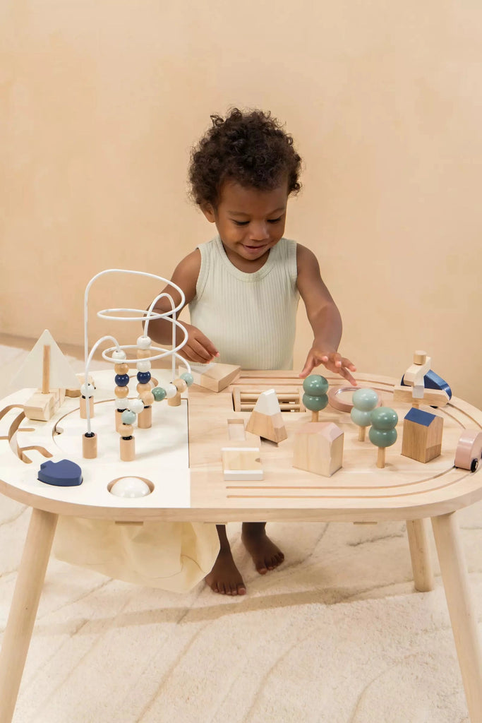 A young child playing with various birch plywood toys on a Wooden Activity Table, focusing intently on arranging blocks and interacting with a bead maze.