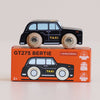 A black cab wooden taxi labeled “TAXI” rests on an orange box featuring the same car design. The box is printed with “No. 45 GT275 Bertie | Made in England” and displays icons for sustainable wood, child safe paints, and Made in England, making this London toy car a charming and safe addition to any playroom.