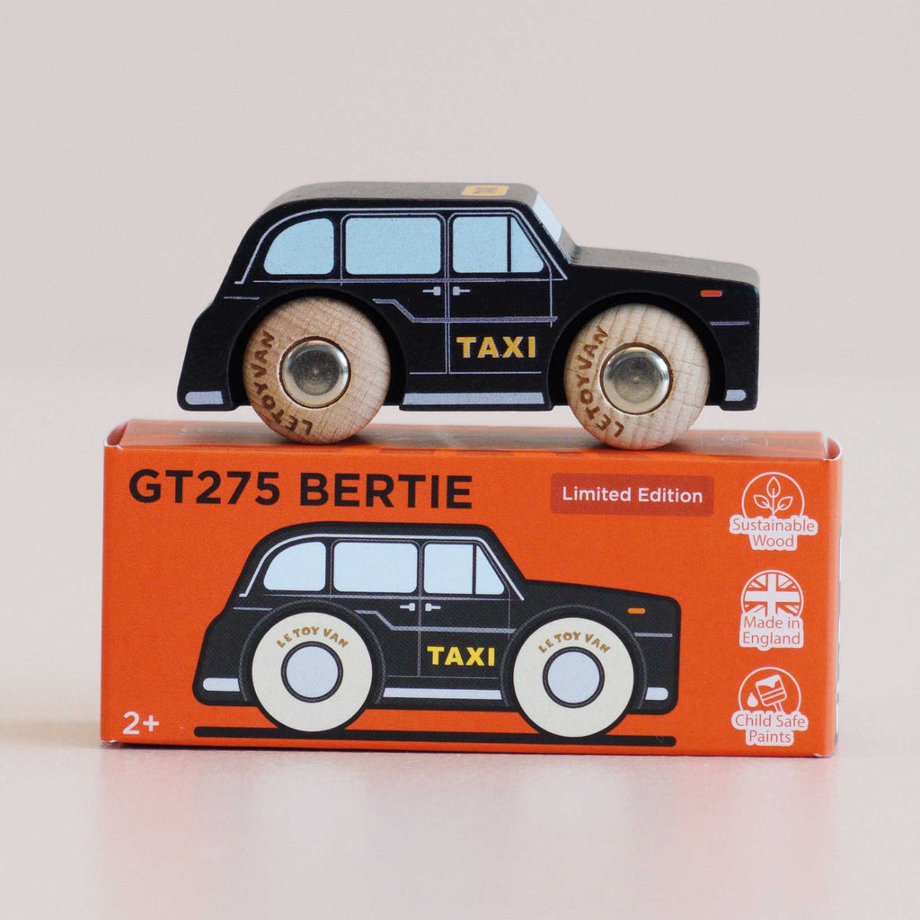 A black cab wooden taxi labeled “TAXI” rests on an orange box featuring the same car design. The box is printed with “No. 45 GT275 Bertie | Made in England” and displays icons for sustainable wood, child safe paints, and Made in England, making this London toy car a charming and safe addition to any playroom.