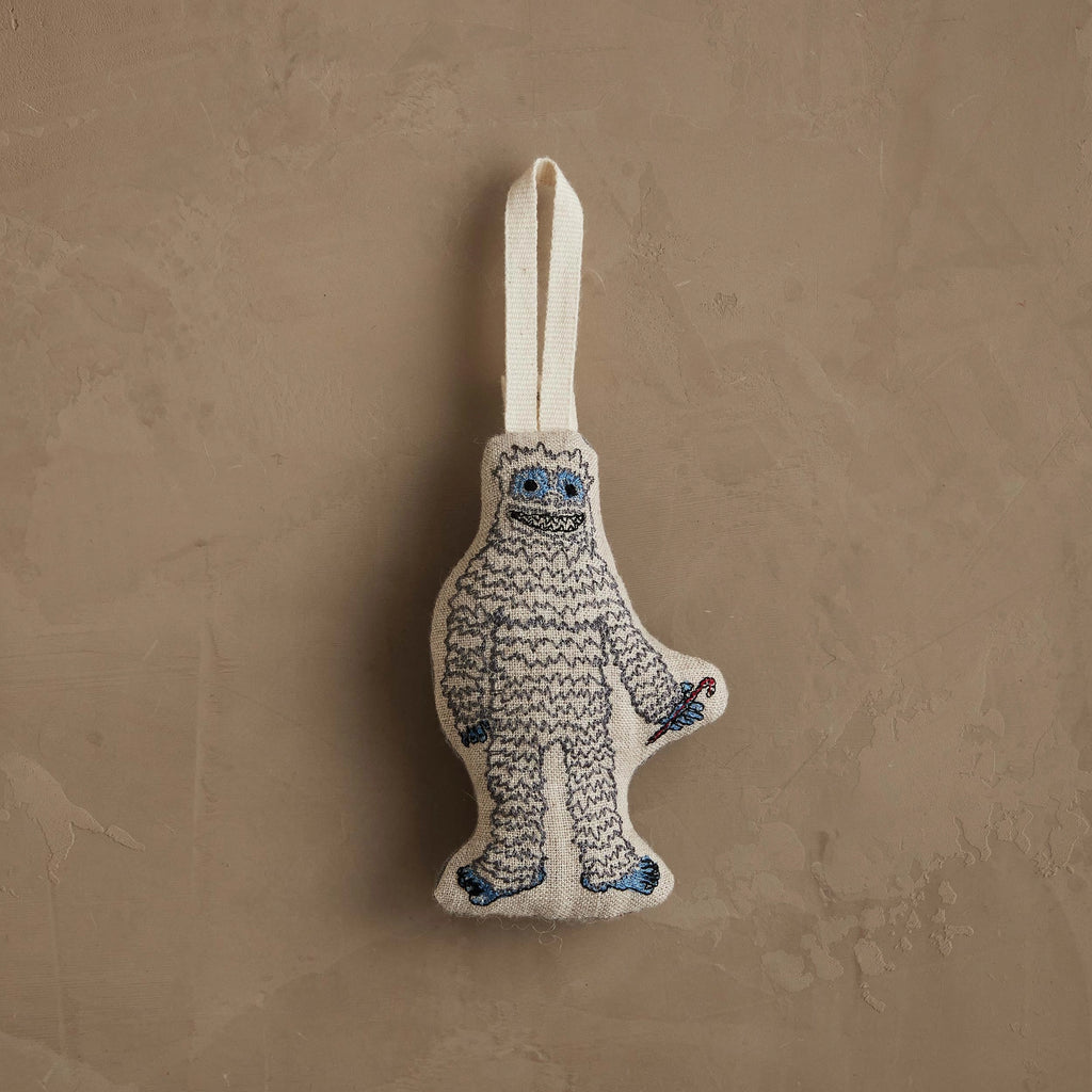 The Coral & Tusk Yeti with Candy Cane Ornament, featuring white fur, blue details, and a candy cane, hangs by a white loop—perfect as a charming Christmas decoration or whimsical gift.