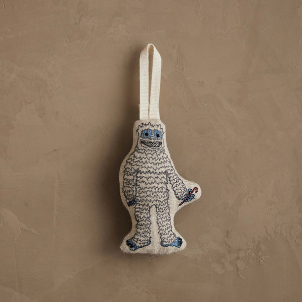 The Coral & Tusk Yeti with Candy Cane Ornament, featuring white fur, blue details, and a candy cane, hangs by a white loop—perfect as a charming Christmas decoration or whimsical gift.