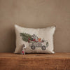 The Coral & Tusk Christmas Tree Car Pocket Pillow features embroidered woodland animals driving a car with a tree and gifts. A small bear figure holding a candy cane is in front—both make charming holiday decor on any wooden surface.