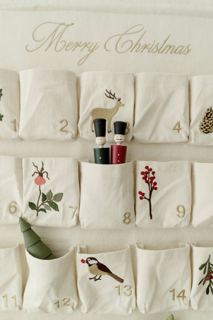 The Sabo Concept Christmas Cotton Advent Calendar features numbered pockets with festive images—deer, pinecone, tree, and bird—and includes two wooden peg dolls plus a small deer figure in pocket number 8.