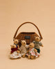 Four Little Forest Animals — The Thompson Family, dressed in charming floral and knit outfits reminiscent of handcrafted family dolls, sit together before a brown wicker basket with a handle, set against a plain tan background.