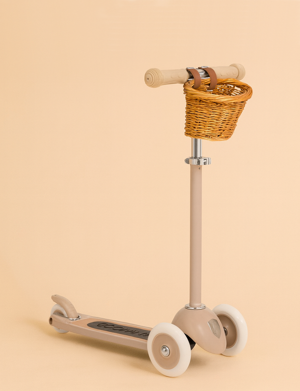 The Banwood Scooter - Beige (New Color) features three white wheels, a small brown wicker basket on the T-handlebar, and an adjustable handlebar for comfort. Ideal among scooters for kids, it's shown against a light beige background.
