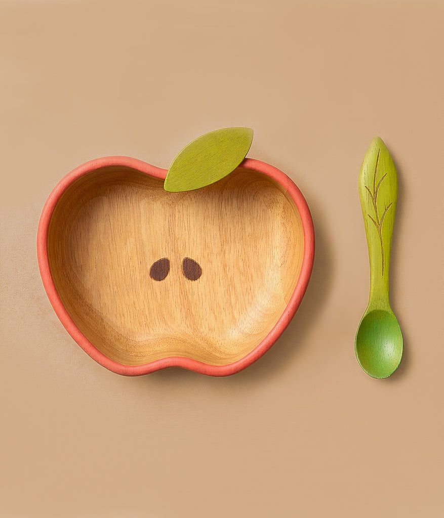The Pepa the Apple Bowl & Spoon Set features a wooden apple-shaped bowl with green leaf detail and seed designs, plus a matching green spoon with leaf pattern—an adorable, non-toxic Hevea wood baby tableware set on a beige background.