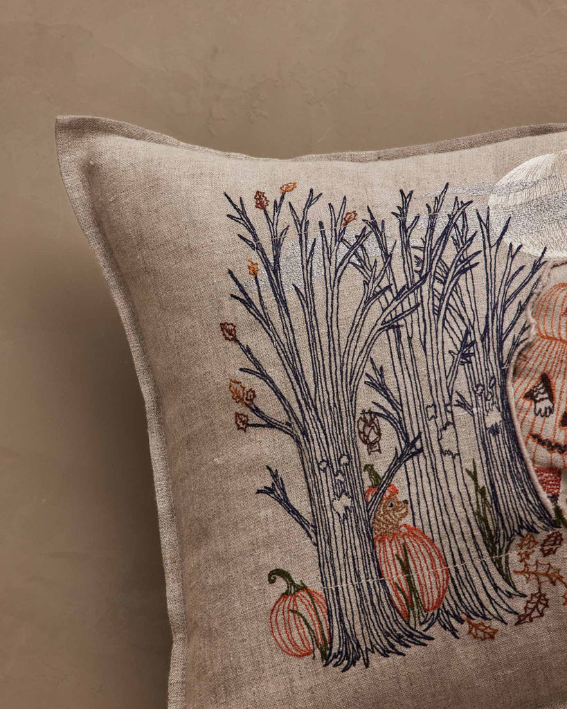 The Coral & Tusk Spooky Forest Pocket Pillow features embroidered leafless trees, pumpkins, and a hidden animal peeking through branches on a beige linen background.