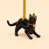 Introducing the Black Cat Cake Topper - Final Sale: This hand-painted porcelain collectible features a black cat crouched with its tail up, wearing a small green and yellow party hat and a red collar adorned with a gold bell. The cat holds a yellow candle on its back, making it a charming cake topper and perfect keepsake birthday gift.