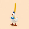 Introducing the Blue Goose Cake Topper - Final Sale: this charming porcelain decoration features a ceramic goose wearing a blue party hat and bow tie, carrying a yellow candle on its back, all set against a plain light beige background—a delightful handcrafted birthday keepsake and collectible.