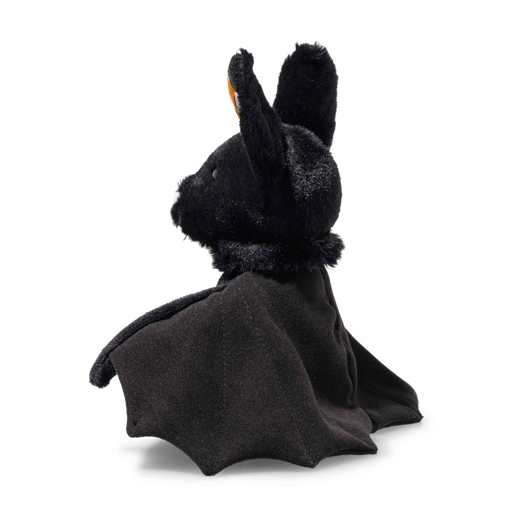 Steiff Boris the Spooky Bat sits upright, covered in soft black fabric with large pointed ears and outstretched wings—making it a charming Halloween decoration—shown against a white background.