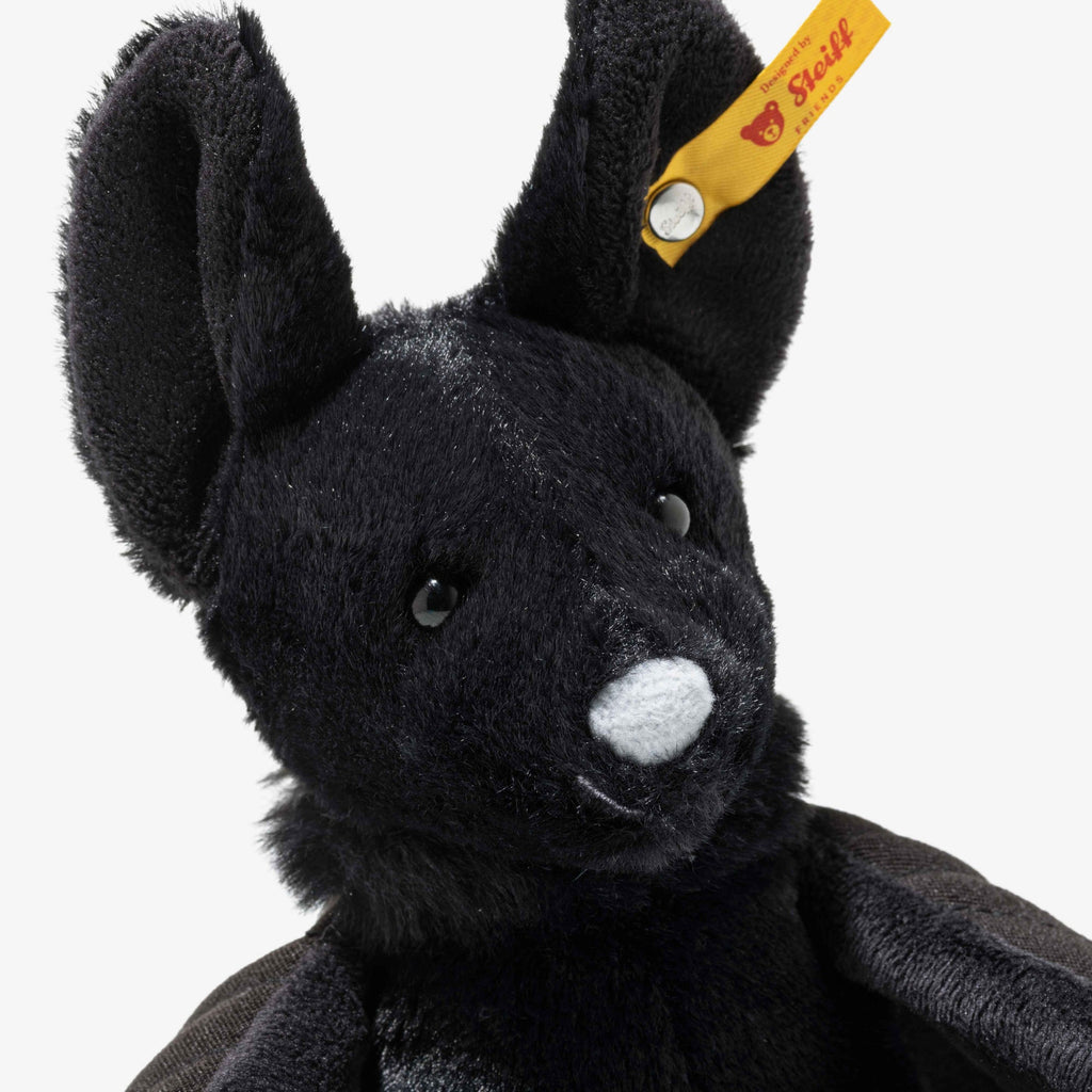 A close-up of Steiff Boris the Spooky Bat, a black plush toy with large ears, shiny black eyes, a gray nose, and a yellow Steiff tag—perfect as a festive Halloween decoration or collectible plush.