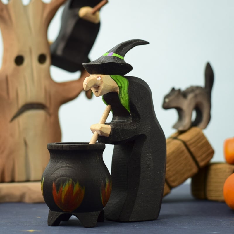 The Bumbu Handmade Wooden Brewing Witch and Cauldron Set includes a green-haired witch, cauldron, tree with a face, black cat, and pumpkins—perfect for imaginative and Montessori-inspired Halloween play.