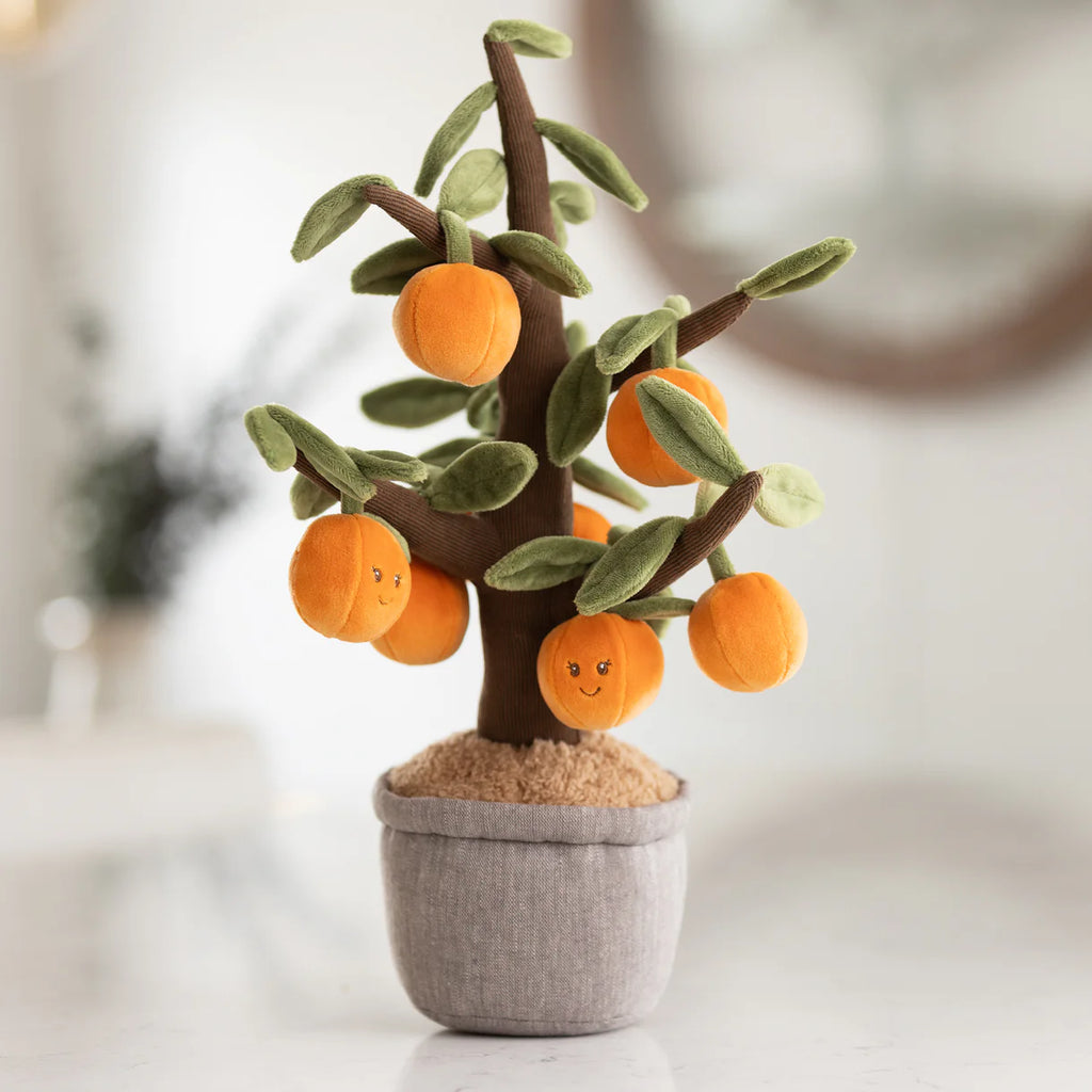 The Bukowski - Orange Tree features green leaves and smiling orange fruit in a gray fabric pot, making it perfect for imaginative play or as a cuddly companion.