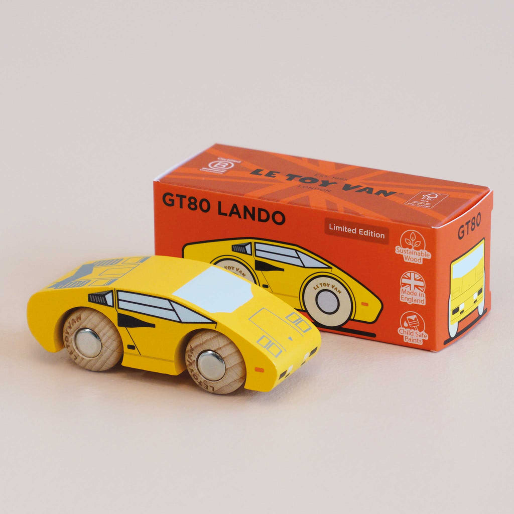 A yellow wooden supercar toy car, labeled No. 14 GT80 Lando and made in England, is displayed in front of its matching orange and red box adorned with illustrations and product information, featuring a child-safe finish for safe play.