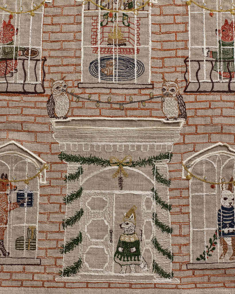 Coral & Tusk Holiday House Advent Calendar featuring an embroidered linen brick house facade filled with festive animals, including owls on a mantelpiece and a party-hat-wearing dog at the front door.