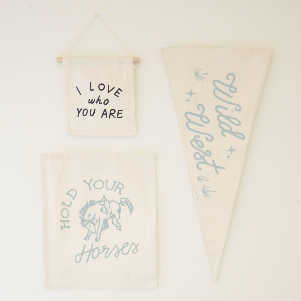 The "I Love Who You Are" Natural Canvas Sign is a cream-colored, handmade wall hanging—perfect as unique Kenyan artisan decor or an inspirational accent to any space.