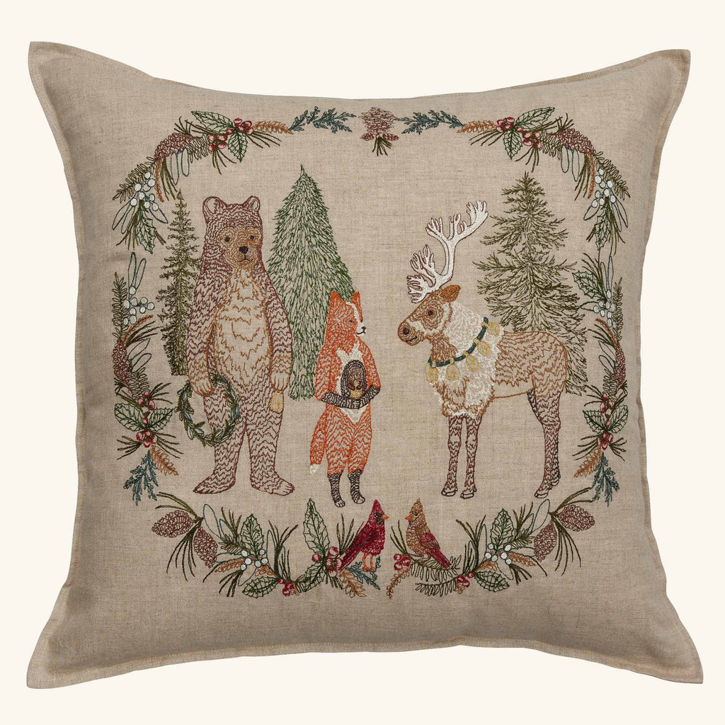 Coral & Tusk Christmas Cheer Wreath Pillow, a square embroidered linen pillow featuring a bear, fox, and reindeer surrounded by a holiday wreath of pine branches, berries, and two cardinals.