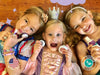 Three young girls wearing tiaras and princess dresses hold a Klee Naturals Deluxe Makeup Kit - Regal Queen Fairy while smiling at the camera.