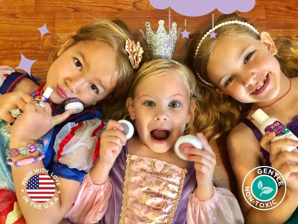 Three young girls wearing tiaras and princess dresses hold a Klee Naturals Deluxe Makeup Kit - Regal Queen Fairy while smiling at the camera.