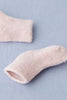 A close-up of a soft, fuzzy Baby Pile Knit Sock - Pink lying on a light blue fabric surface. Another matching pink sock is partially visible in the upper left corner of the image. The fluffy socks appear warm and cozy, suitable for keeping feet warm and comfortable.