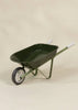 The Heritage Wheelbarrow – Liane, a green children’s wheelbarrow with white handles and a black-and-white wheel, is set against a light beige background—ideal for kids’ outdoor gardening activities.
