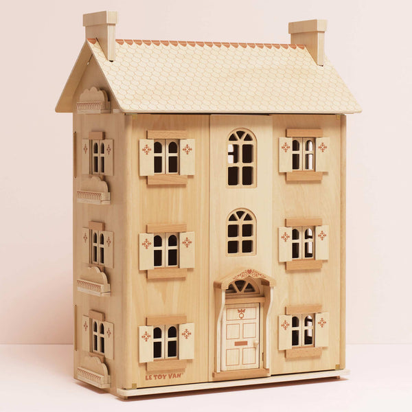 The Grand Natural Wood Doll House is crafted from sustainable wood, with two chimneys, four windows per floor, decorative shutters, a detailed front door, etched details, and "Le Toy Van" branding—perfect for imaginative play.