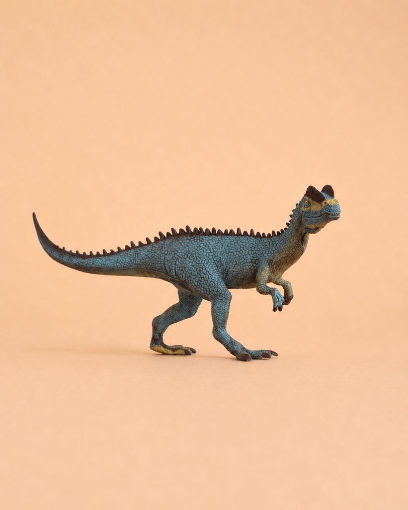 The Schleich Dilophosaurus, a small blue and green dinosaur figurine with a ridged back and short arms from the DINOSAURS collection, stands on a plain peach background, capturing the charm of prehistoric giants.