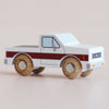 The No. 30 GT165 Charlie, a small wooden pick-up truck featuring a white body, red stripe, and natural wood wheels, made in England, is displayed on a light surface.