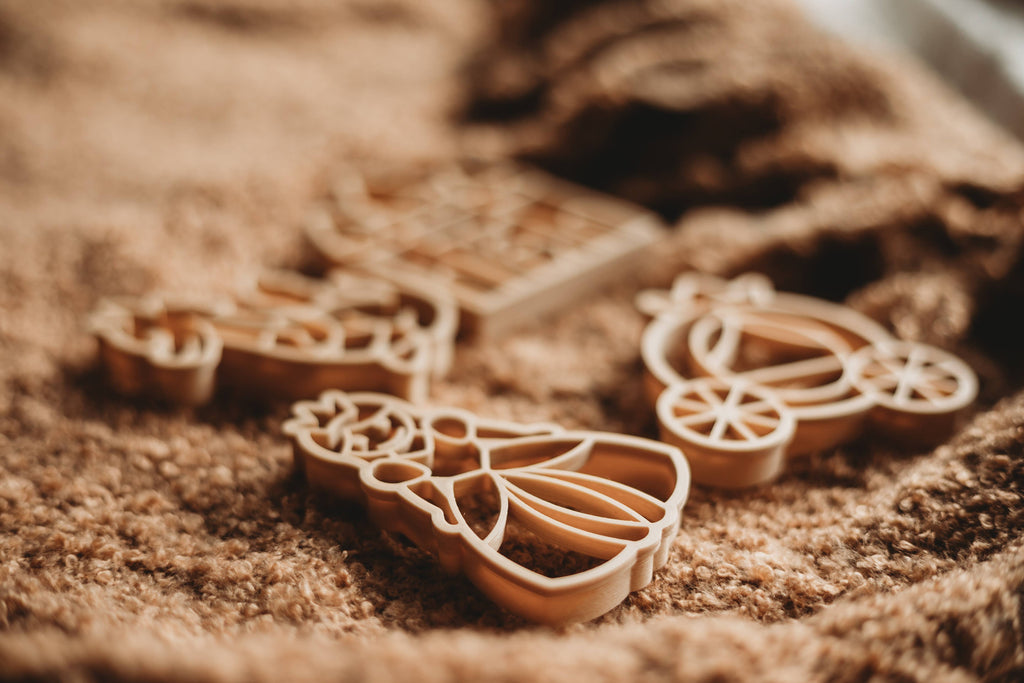 The Princess Cutter Set - Eco Playdough Tool, featuring whimsical shapes like a princess and carriage, rests on a brown textured fabric in softly focused light, highlighting the enchanting fairy-tale designs.