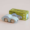 A light blue wooden toy car, No. 2 GT15 Jude | Made in England, sits in front of its matching green box adorned with coordinating artwork and limited edition details. This charming vintage-inspired toy makes a delightful gift for children, with both the car and its box displayed on a light-colored surface.