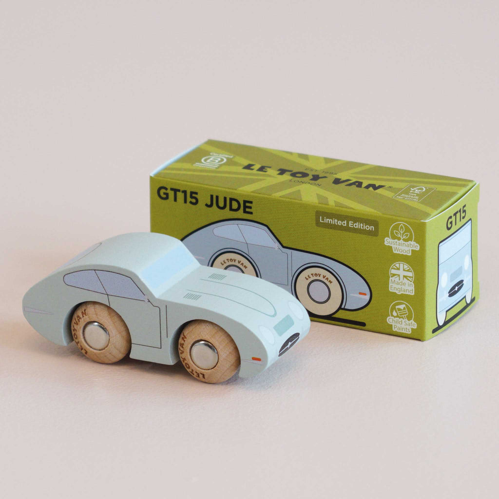 A light blue wooden toy car, No. 2 GT15 Jude | Made in England, sits in front of its matching green box adorned with coordinating artwork and limited edition details. This charming vintage-inspired toy makes a delightful gift for children, with both the car and its box displayed on a light-colored surface.
