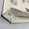 A close-up of light beige folded fabric features colorful feline faces, with visible texture on a gray surface, suggesting its use in crafting a charming Cats Tote Bag or an inside pocket for your next creative project.