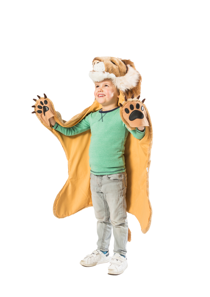A smiling child in a green shirt, jeans, and white sneakers wears the Costume - Lion with a faux fur lion hood and cape with paw mittens, standing on a white background.
