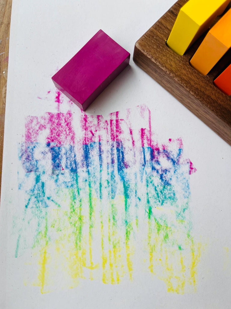 Colorful pastel art created by rubbing a block of pink pastel over a textured surface, next to a Wooden Crayon Holder 8 Stick / 8 Block on a walnut crayon holder.