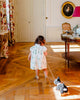 A young child in a white dress develops gross motor skills as she pulls Pull-Along Walter, a black pull-along toy dog on wooden wheels, through an elegant, sunlit room with wooden floors and classic decor.