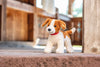 A Steiff, Snuffy Dog Plush Puppy, 11" with brown and white fur and a red collar, sitting on a concrete step with a blurred wooden background.