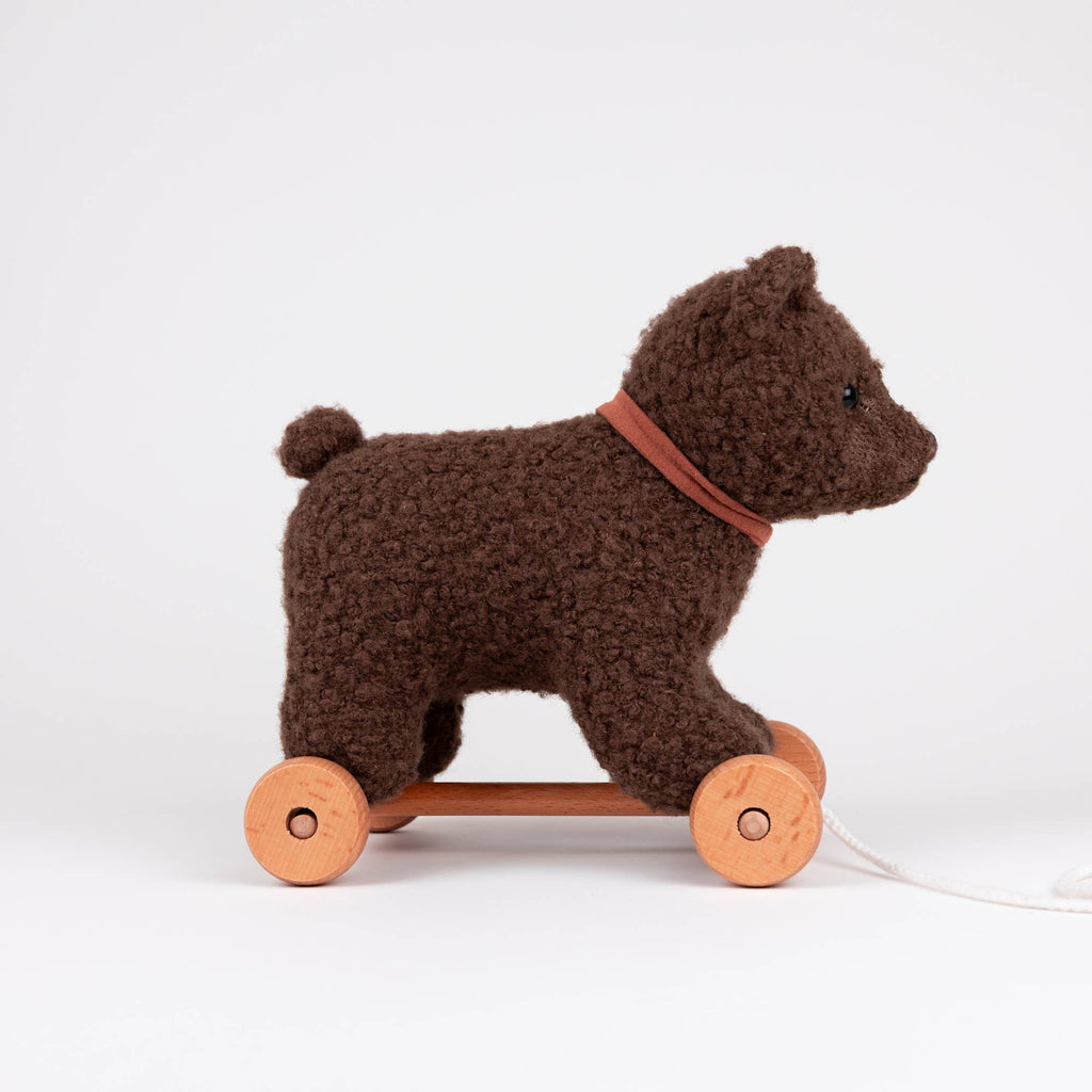 A brown, plush Pull-Along Raoul bear from Egmont Toys, featuring wooden wheels, a pull string, a small tail, and a simple collar, is shown against a plain white background.