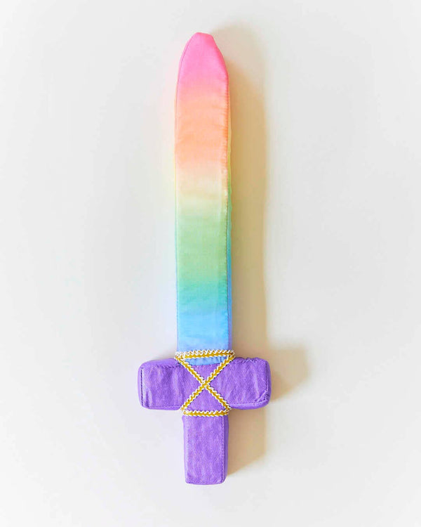 Introducing Sarah's Silk Soft Sword: a captivating plush toy featuring a silky gradient rainbow blade and a purple hilt adorned with intricate yellow stitching. Ideal for imaginative play, this striking soft sword is beautifully displayed against a plain white backdrop.