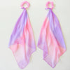 The Easter Basket Gift Set features two pink scrunchies, each adorned with a long ombre scarf transitioning from pink to lavender, reminiscent of a delicate ballet suit and set against a simple light background.