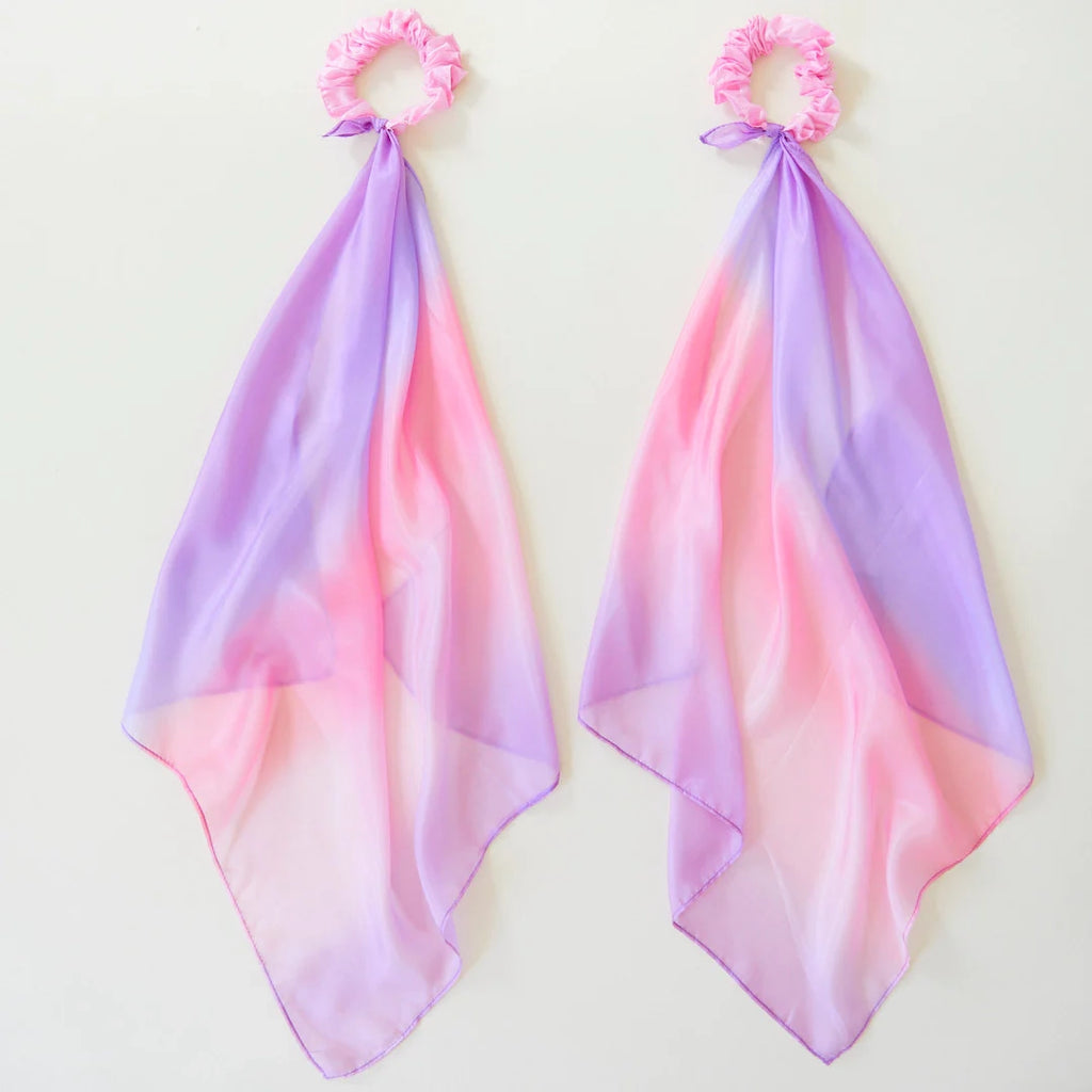 The Easter Basket Gift Set features two pink scrunchies, each adorned with a long ombre scarf transitioning from pink to lavender, reminiscent of a delicate ballet suit and set against a simple light background.