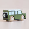 Introducing the No. 27 GT150 Archie, a small green wooden 4x4 toy car handcrafted in England, featuring black and white wheels, a black spare tire mounted at the back, and a distinctive white roof. Photographed on a neutral surface, it’s perfect for timeless imaginative play.