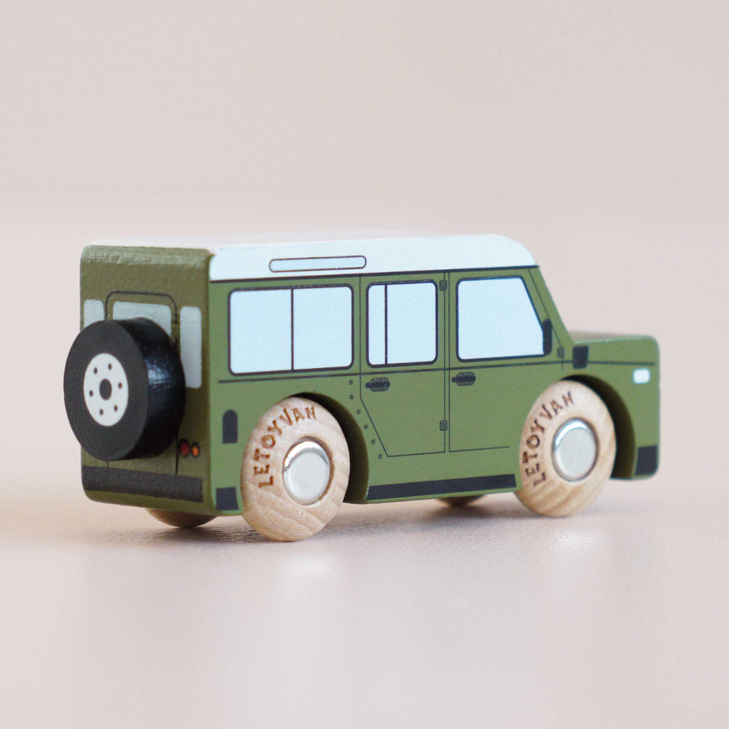 Introducing the No. 27 GT150 Archie, a small green wooden 4x4 toy car handcrafted in England, featuring black and white wheels, a black spare tire mounted at the back, and a distinctive white roof. Photographed on a neutral surface, it’s perfect for timeless imaginative play.