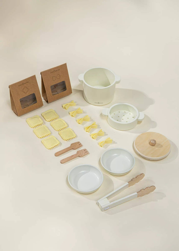 The Wooden Pasta Playset is thoughtfully organized with toy kitchen items, including a pot, steamer, plates, utensils, tongs, and two cardboard packages that resemble pasta boxes. It's perfect for imaginative play on a light background.