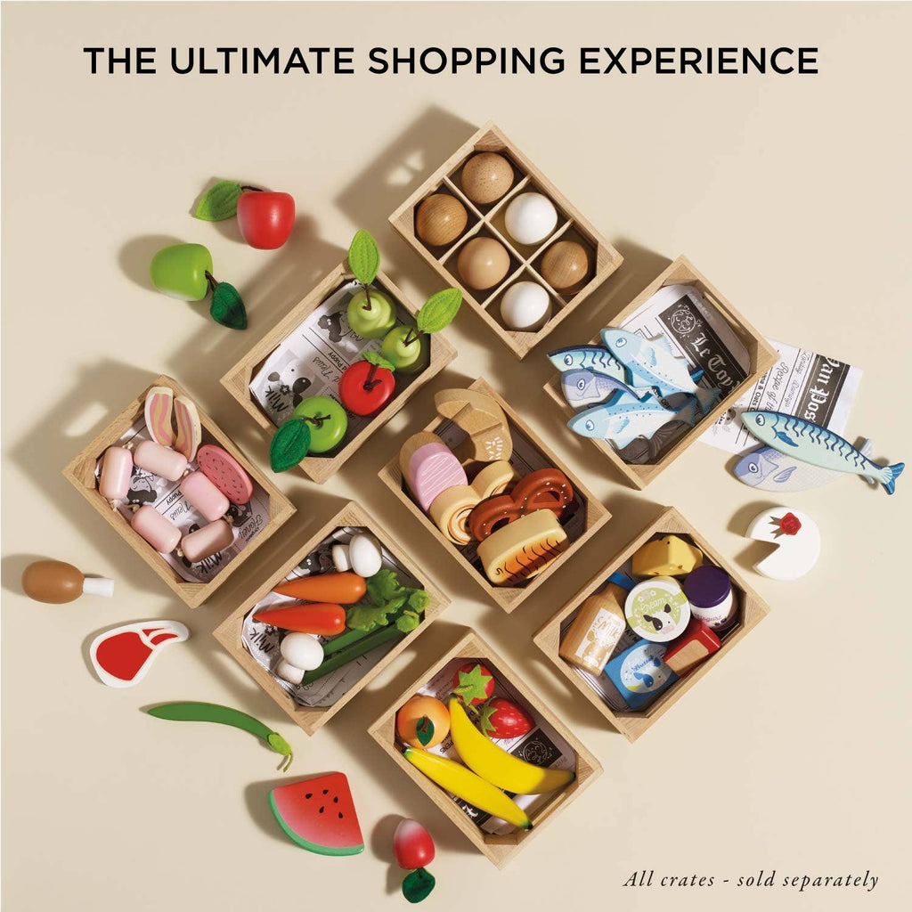 The Bakery & Patisserie Wooden Market Crate, filled with pretend play toy foods like eggs, fish, cheese, and fruits, is neatly arranged on a light surface. Text above reads: “The Ultimate Shopping Experience – Baker's Basket.”.