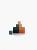 A pyramid of Sabo Concept Mini Wooden Blocks - Tropics—featuring vibrant teal, black, orange, and beige hues—stands stacked against a white background, emphasizing the educational benefits of toys that enhance fine motor skills, while a single teal block rests apart from the main arrangement.