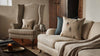 Cozy living room with a beige armchair, matching sofa, textured throw, and the Coral & Tusk Aspen Skiers Pillow for charming winter decor. A lit candle, books, and a tray rest on a rustic wooden table.