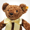 The Steiff Cosy Year Bear 2026 13" is a brown plush teddy with curly fur, shiny black eyes, black nose, pale yellow satin bow, and yellow Steiff ear tag—an ideal New Year 2026 gift—shown against a white background.
