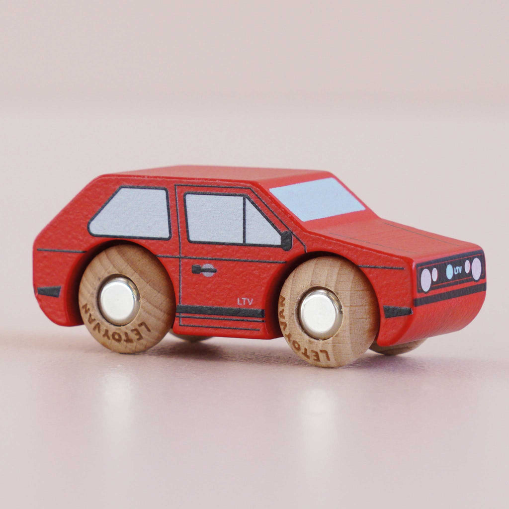 The No. 8 GT50 Gary | Made in England, a small red wooden toy car with vintage charm, featuring black and white details and four natural wood wheels, is placed on a light pink surface.