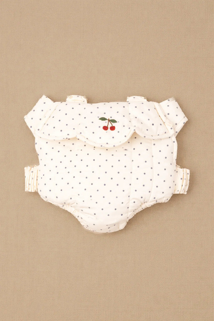 The Konges Sloejd Doll Carrier - Estate Dot is displayed beside a white polka-dotted baby diaper cover with ruffles and an embroidered red cherry design, set against a beige background.