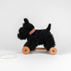Pull-Along Walter, a black plush dog pull-along toy with a red plaid collar, sits on sturdy wooden wheels and features a white pull string—perfect for encouraging gross motor skills through active play.
